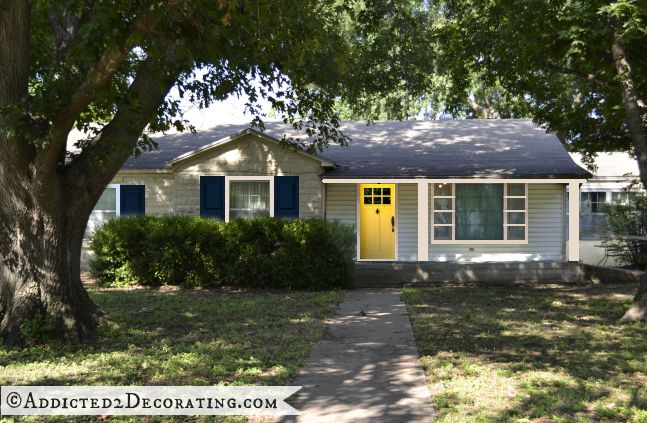 White stone house, yellow front door, navy blue shutters