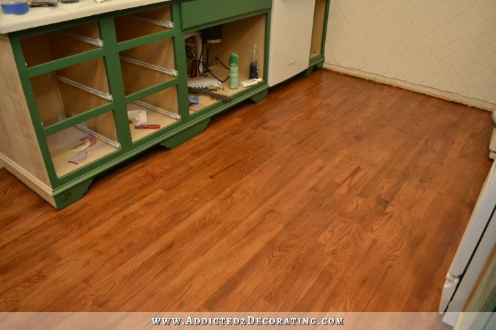 stained red oak floor in kitchen with green cabinets and white subway tile walls
