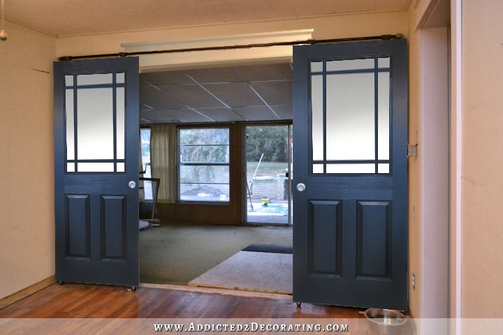 Black rolling barn door style doors with six panes of glass of unequal size on top