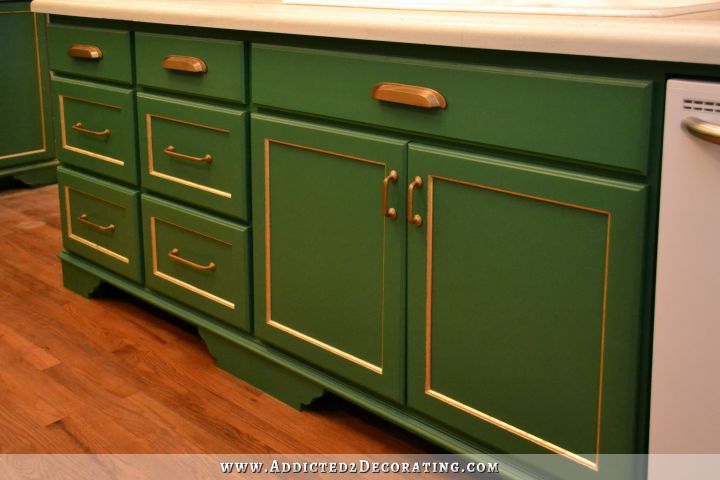 Green kitchen cabinets with gold leaf accents and antique brass hardware, with white concrete countertops