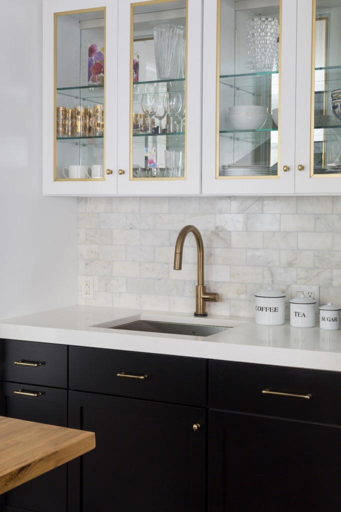 kitchen remodel from Design Manifest, with black lower cabinets, white upper cabinets, and gold trim on glass front doors