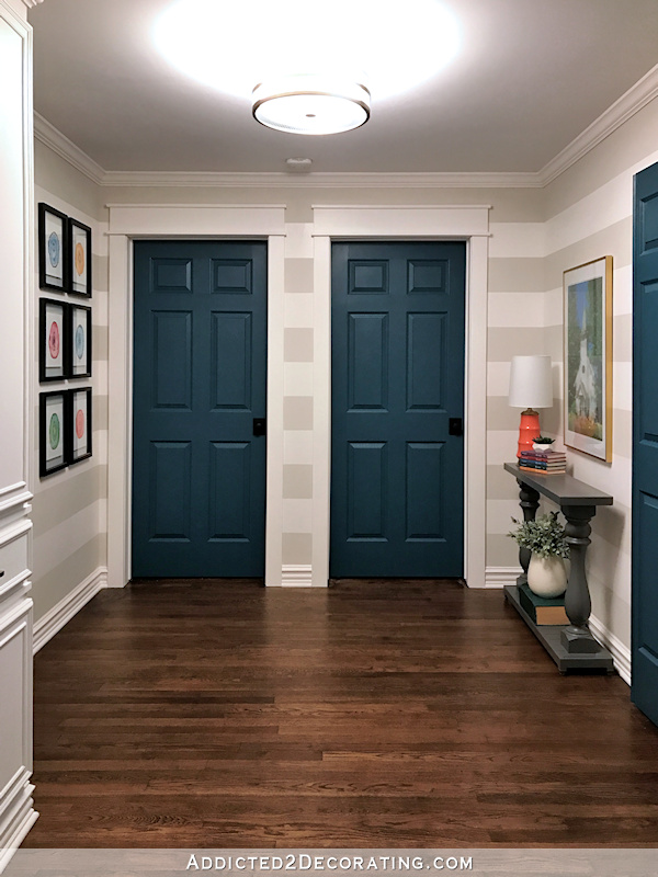 hallway after remodel - original hardwood floors, teal doors, striped walls, watercolor artwork