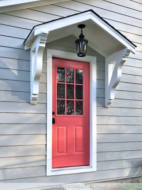 Portico above exterior door with black pendant light and coral door