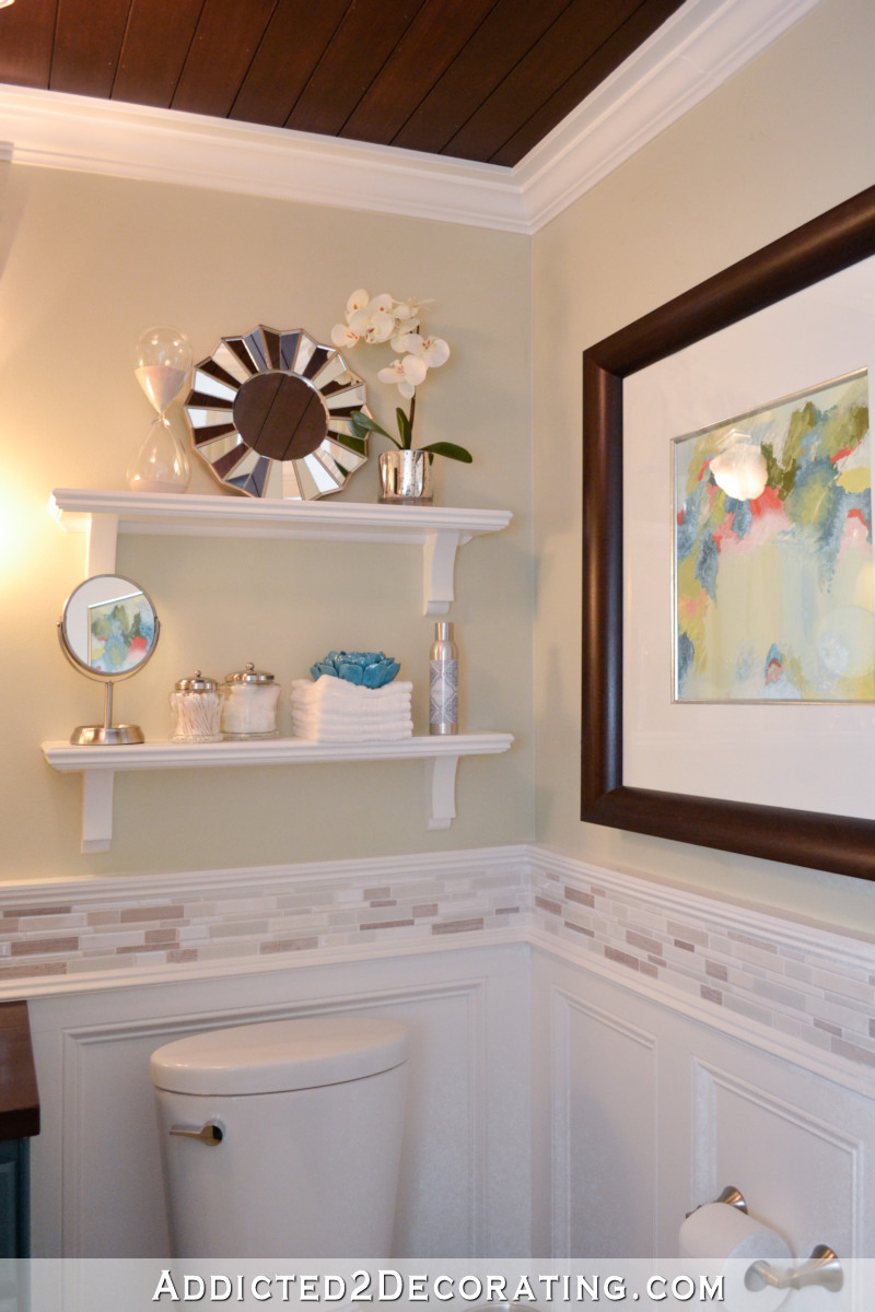 DIY wall shelves above toilet and framed artwork on bathroom wall