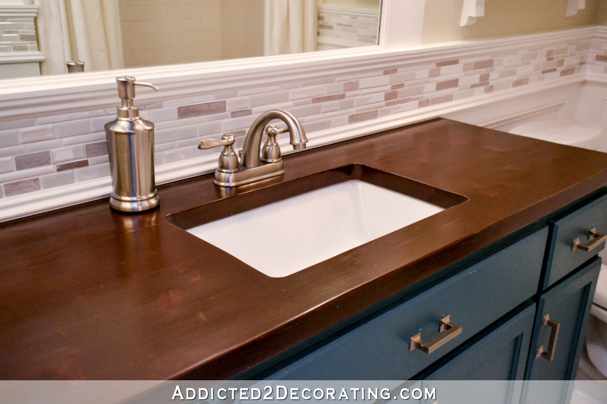 Teal bathroom vanity with dark stained wood countertop and mosaic tile backsplash.