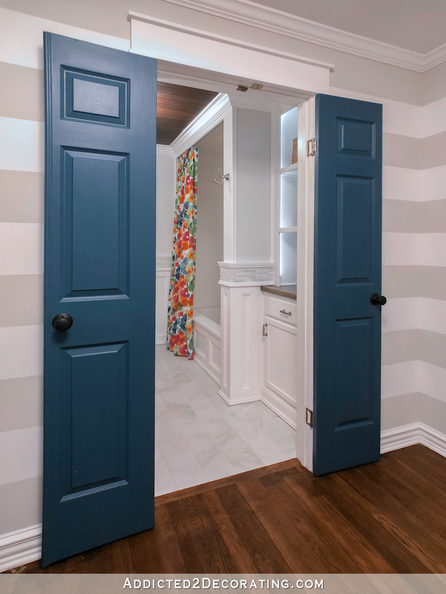 View from hallway with horizontal striped walls into bathroom with colorful floral shower curtain