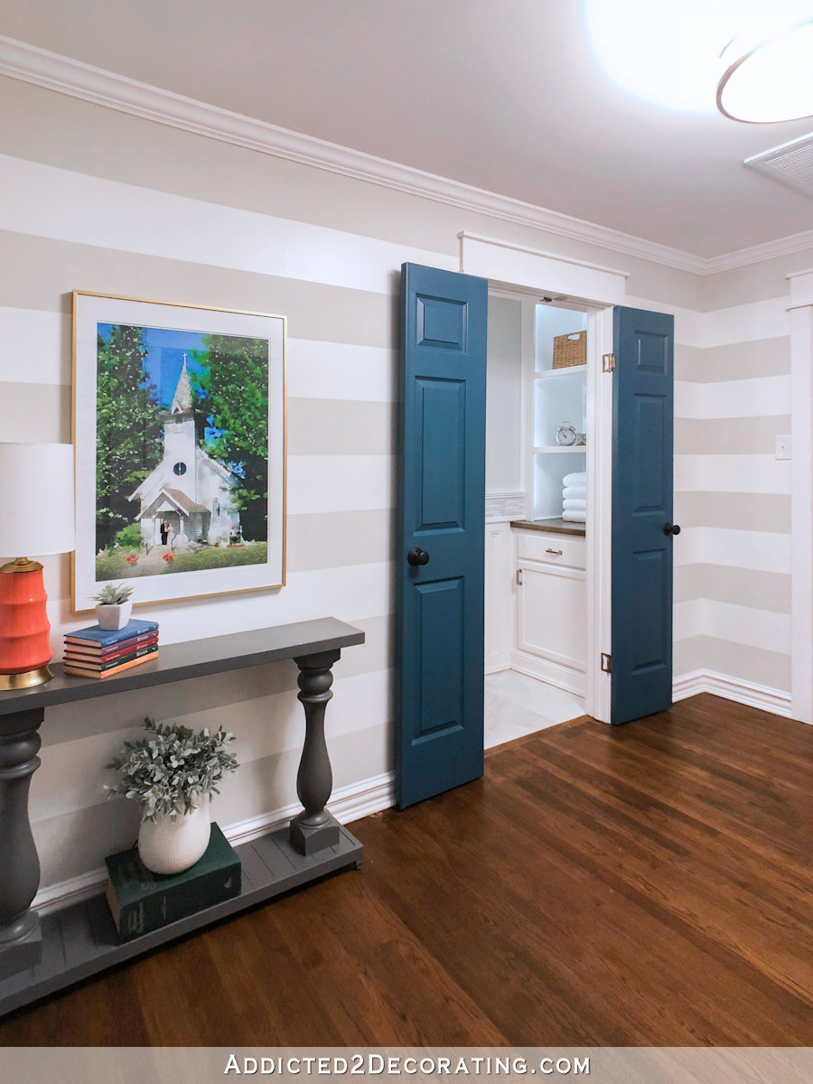 hallway with horizontal striped walls in white and gray, dark teal interior doors, and coral accents
