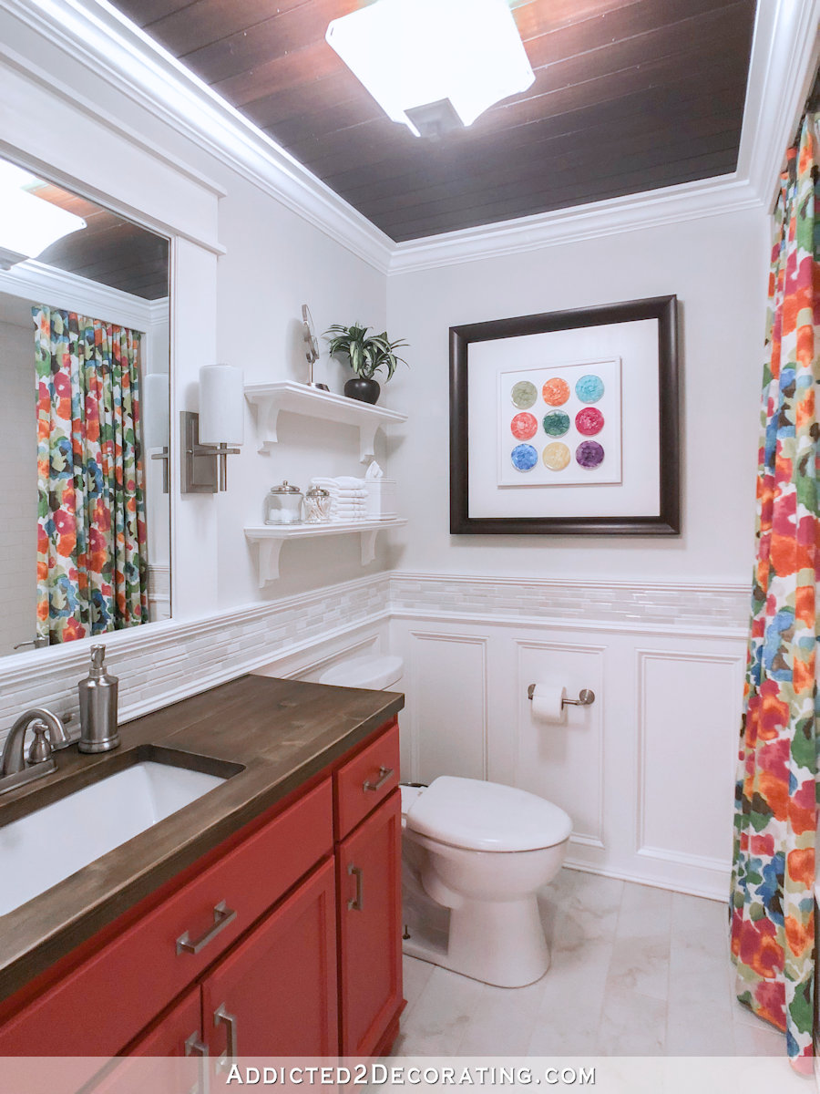 Colorful bathroom makeover with coral vanity, wood countertops, and bright floral shower curtain.