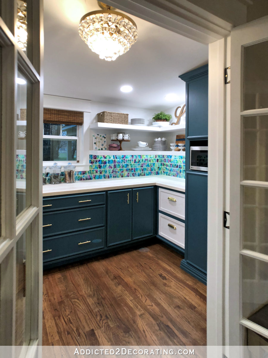 Finished butler's pantry with dark teal cabinets, whitewashed wood countertop, resin tile backsplash, and white open shelves
