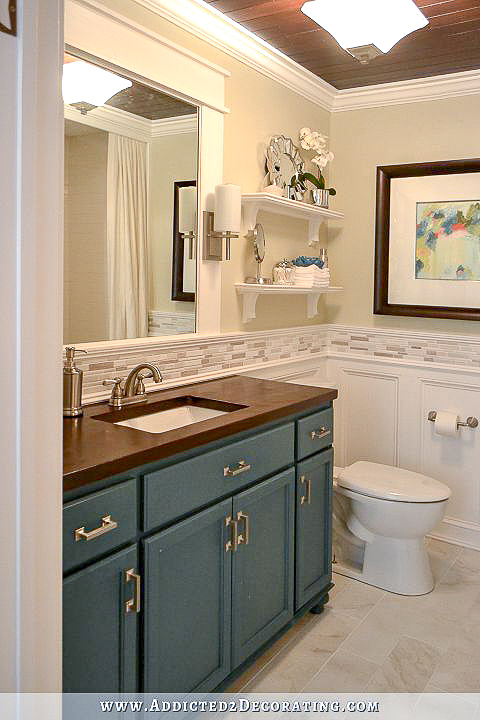 bathroom with teal vanity, light green walls, and white wainscoting with mosaic tile accent