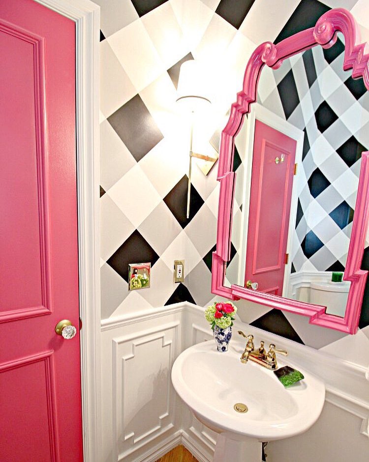 Small bathroom with black and white checked walls, bold pink door and mirror frame, white wainscoting, from Jennifer at Dimples and Tangles (@jenniferdimplesandtangles) in Instagram