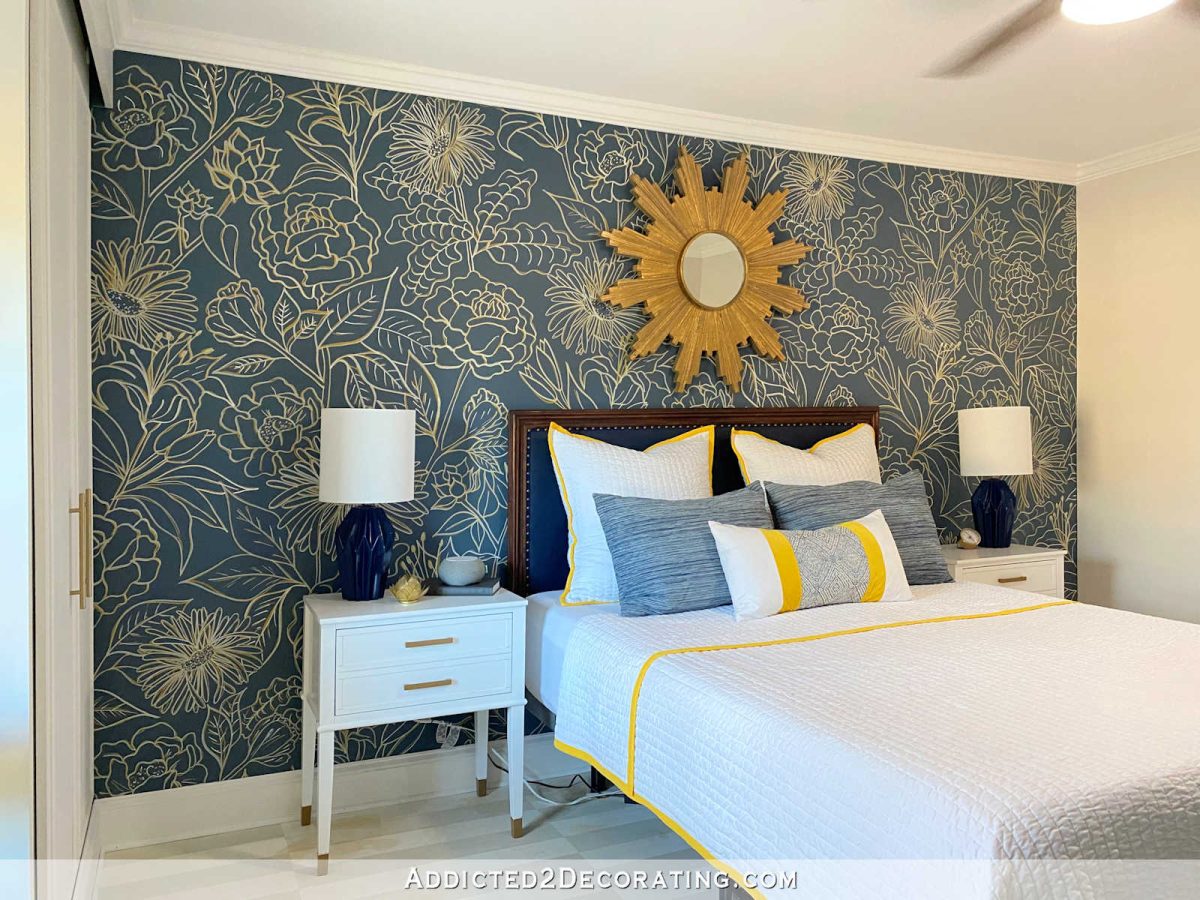 navy blue floral accent wall in bedroom with gold sunburst mirror and upholstered headboard