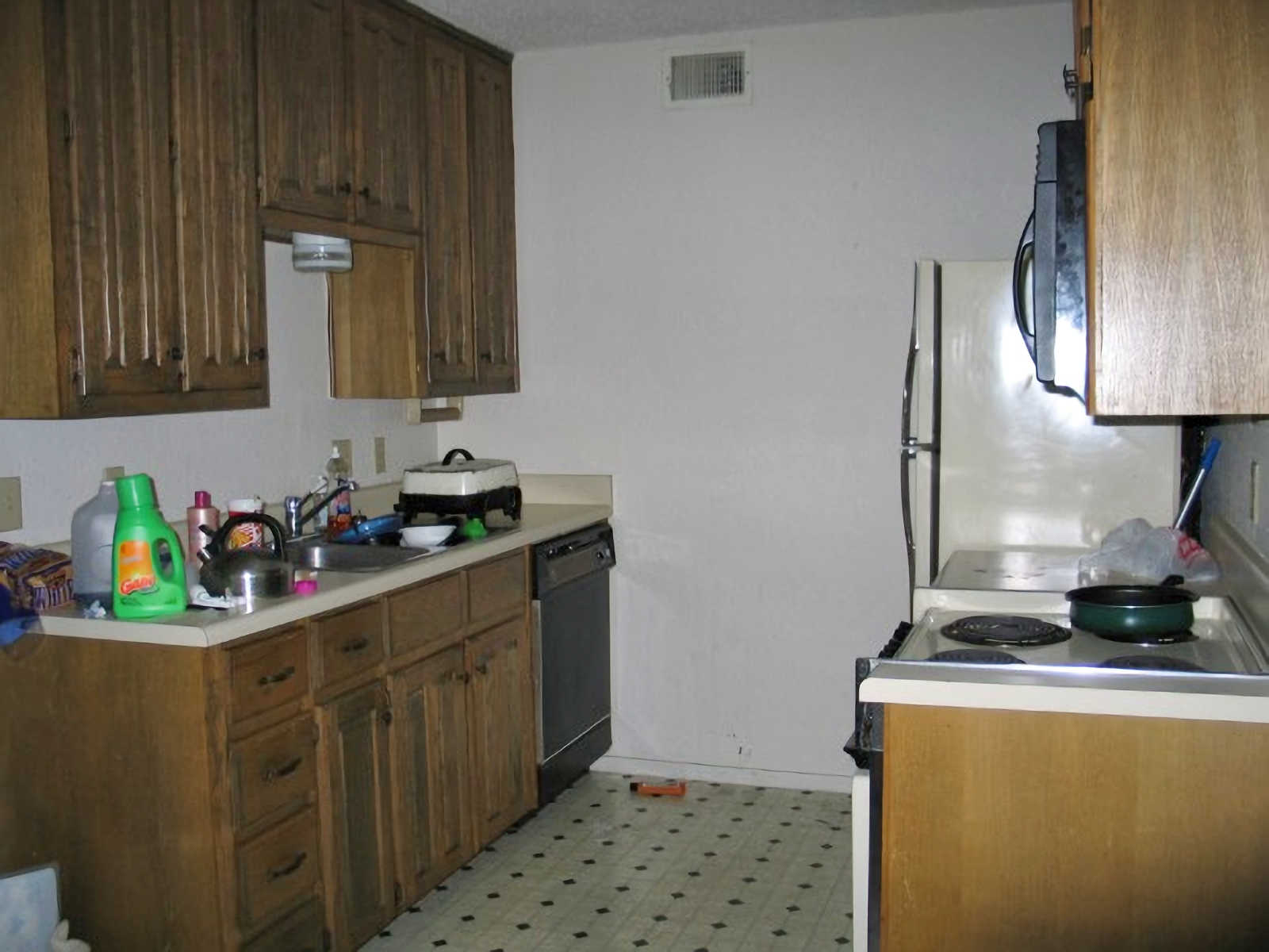 Small condo kitchen before remodel with old laminate countertops, outdated appliances, and stained wood cabinets