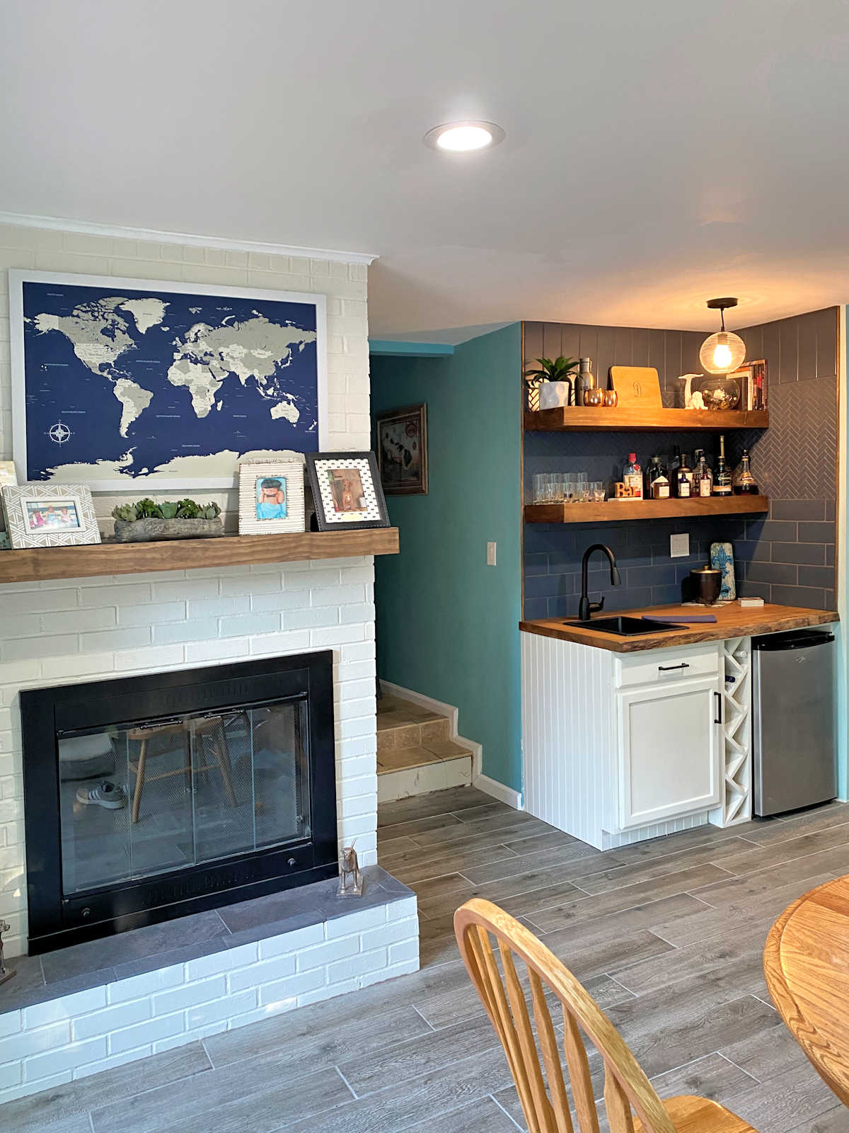 wet bar area in living room with live edge wood countertop, white cabinets, wood floating shelves, and dark blue tiles