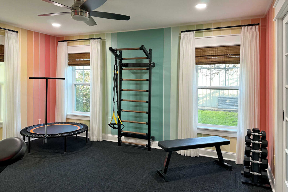 finished home gym with colorful striped walls, black FLOR carpet tiles, white sheer curtains, Swedish ladder, Bellicon rebounder