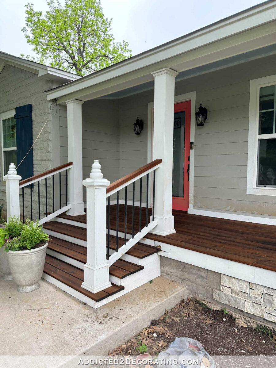 Wood front porch built over a concrete porch, dark stained porch boards, white columns and trim, coral front door