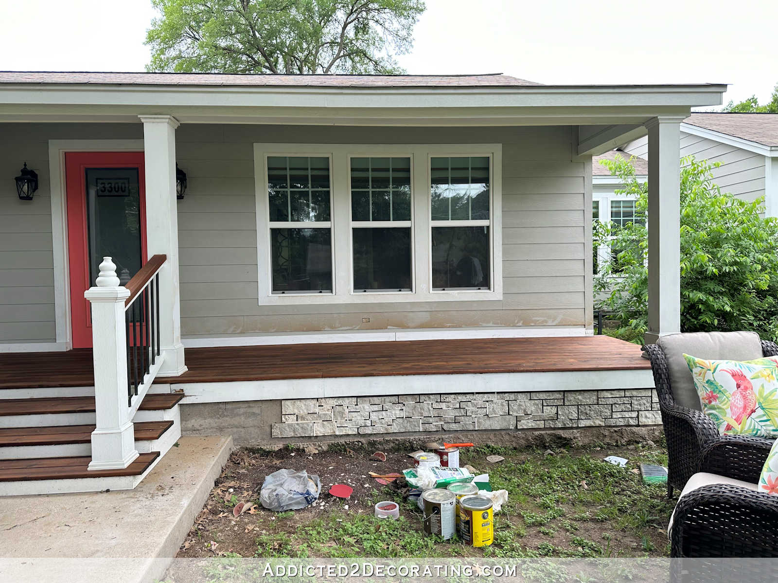 Front porch in progress with stained cedar wood, white trim, light gray siding, coral front door, and faux stone skirting