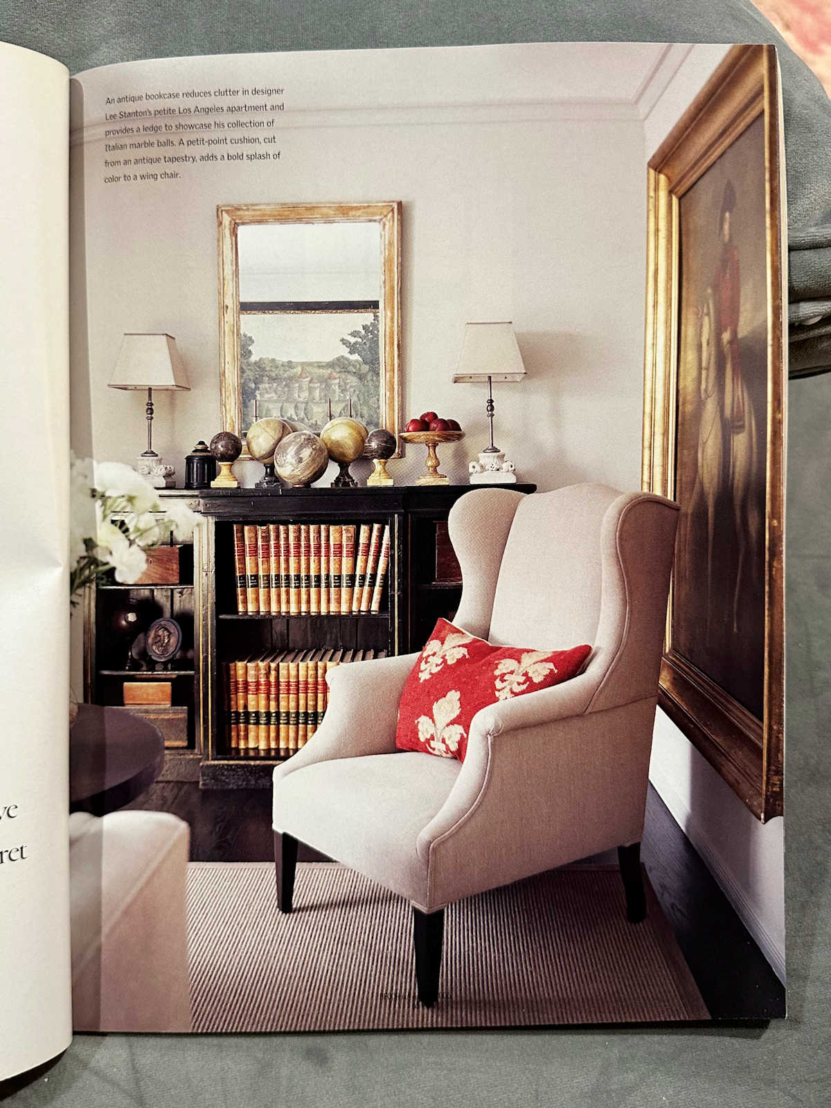 Sitting area with bookshelves, wingback chair, large oil painting with gold gilded frame, collection of globes. 